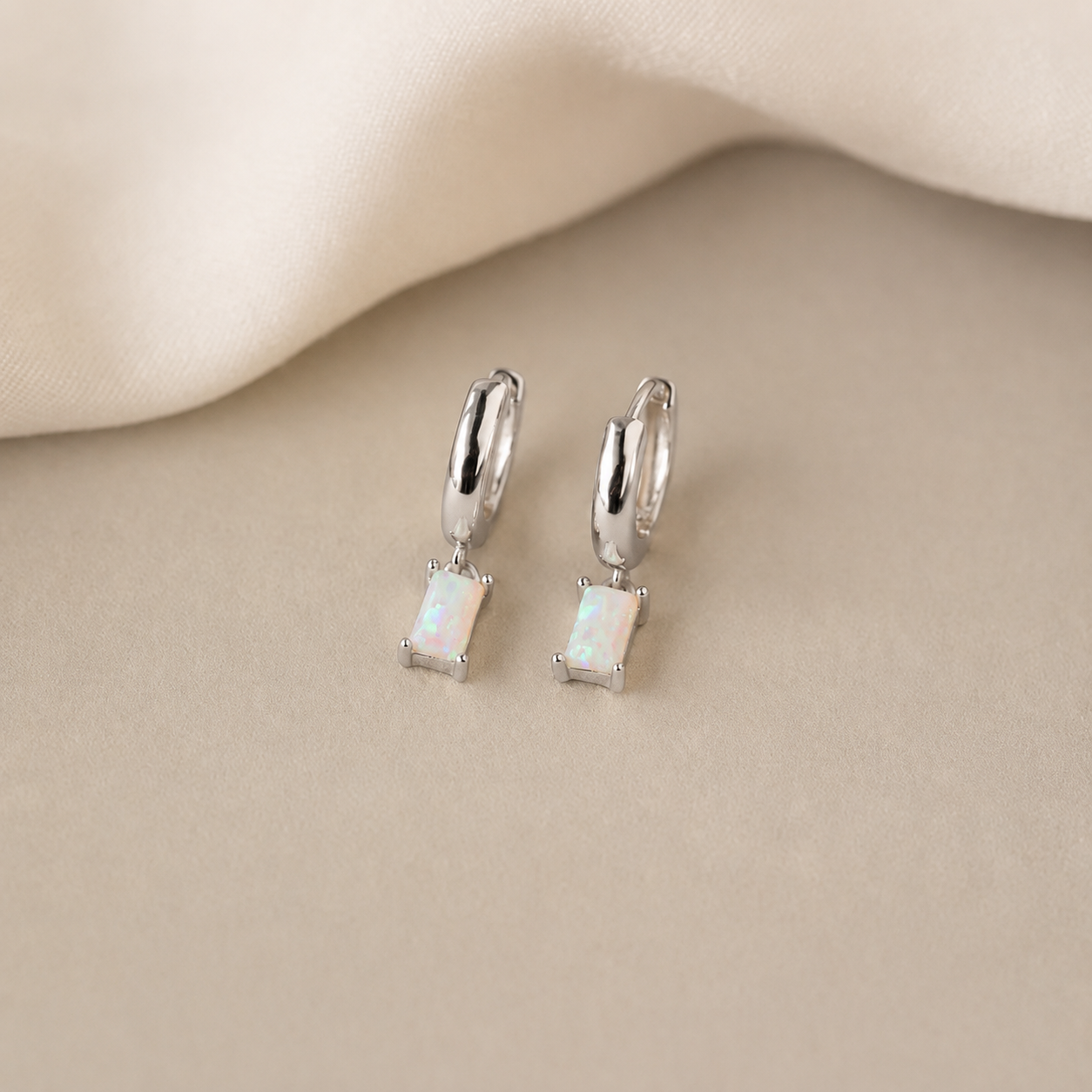 Pair of silver earrings with gemstones on a beige fabric background